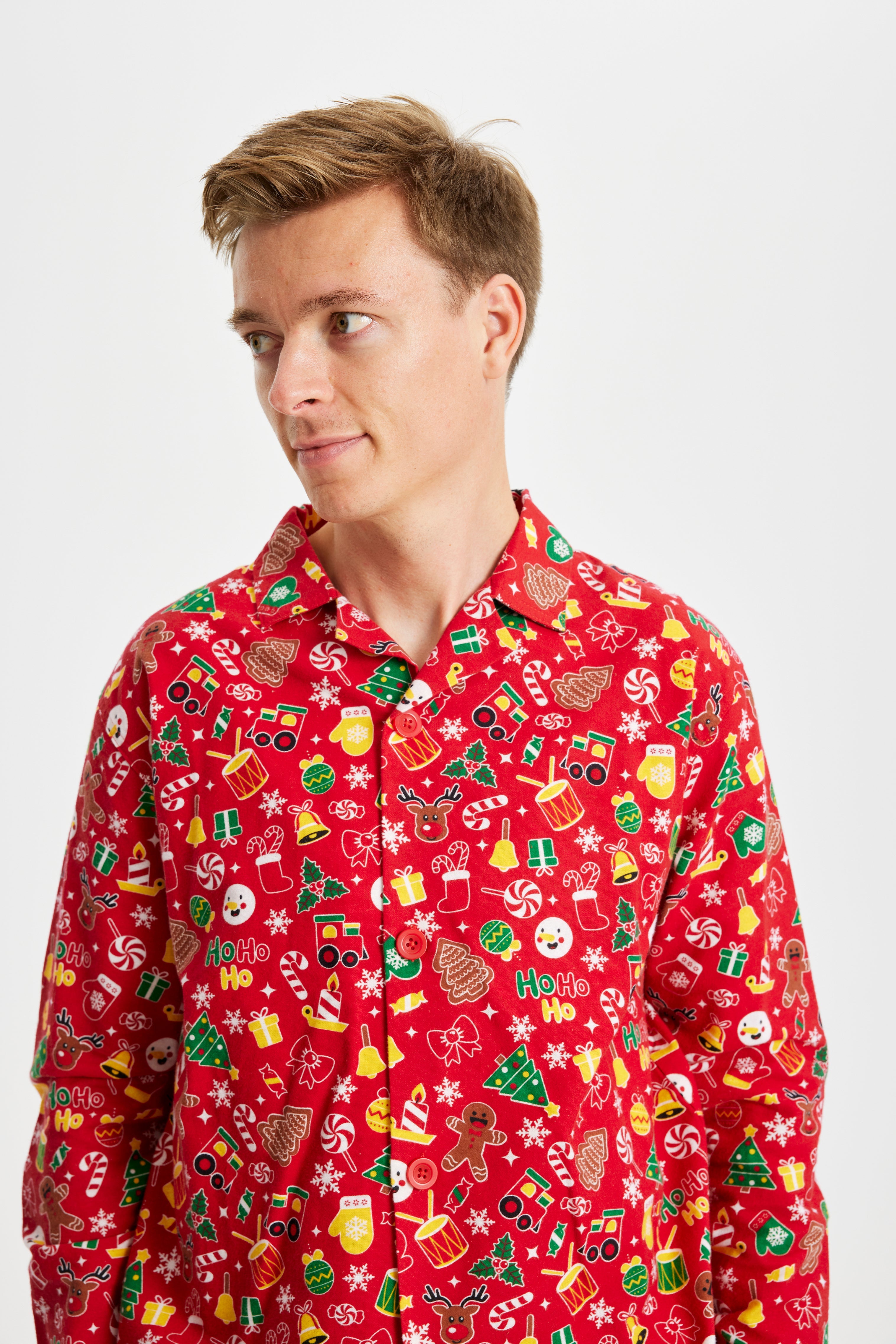 En mand kigger til siden og er iført en postkasserød pyjamas i juletema med masser af forskelligt julepynt på.